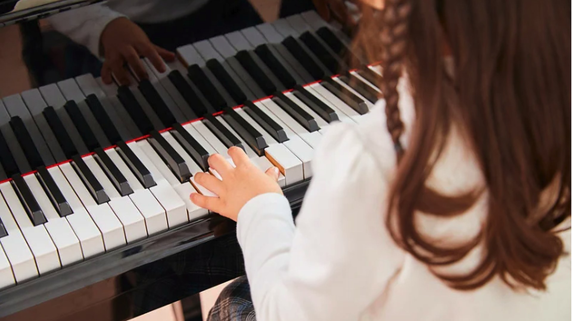 A young girl with a braid seated at a grand piano, her hands resting on the keys during an at-home lesson