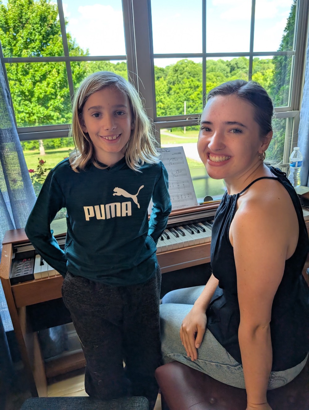 A Grace Haven teacher and her student smiling together at the piano during an at-home lesson