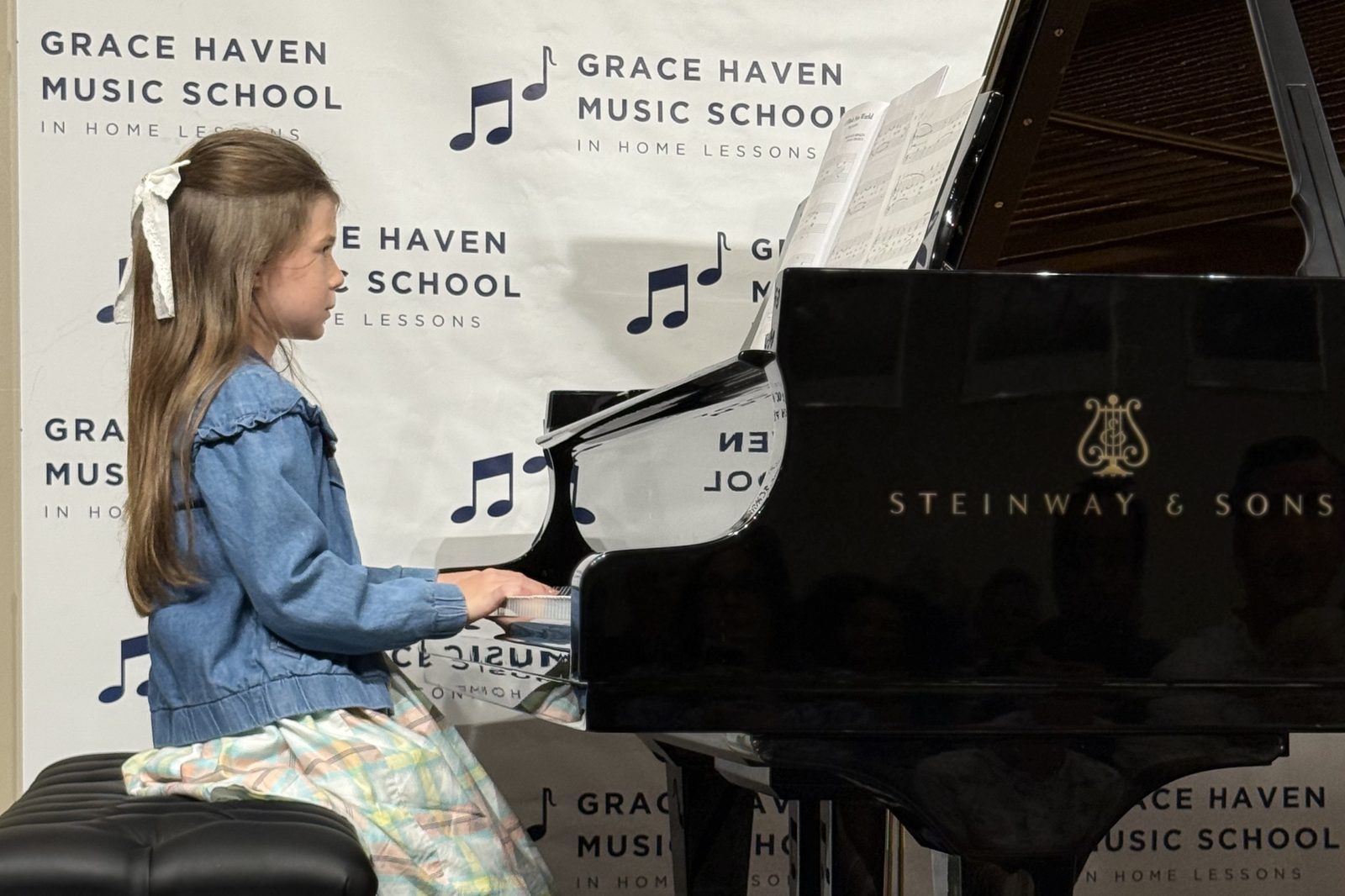 A Grace Haven student playing a grand piano at a recital, in front of a Grace Haven Music School backdrop